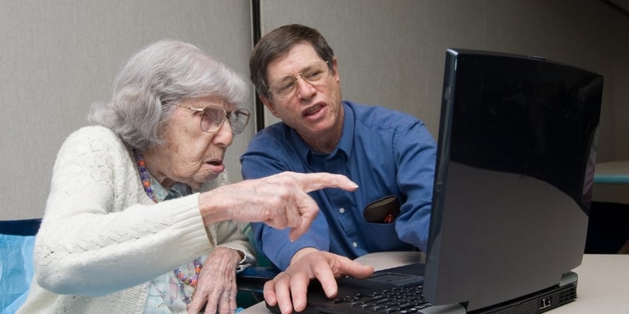 elderly-woman-points-at-computer-while-younger-man-operates-it