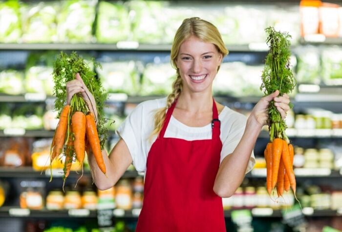 Smiling-female-staff-holding-organic-carrots
