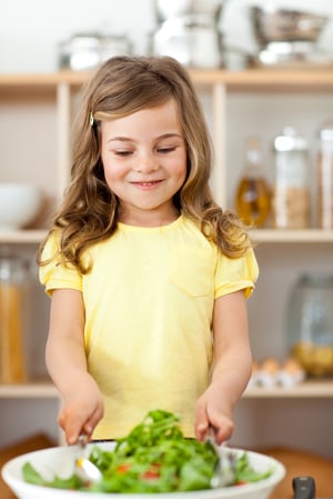 Adorable little child preparing salad in the kitchen