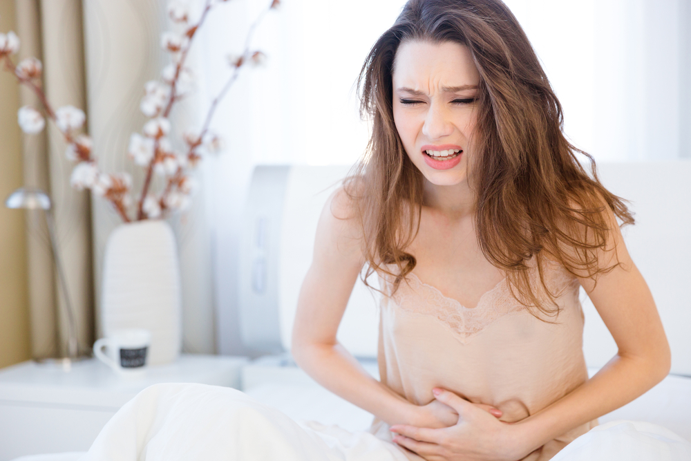 Beautiful young woman in lingerie sitting on bed and suffering from abdominal pain