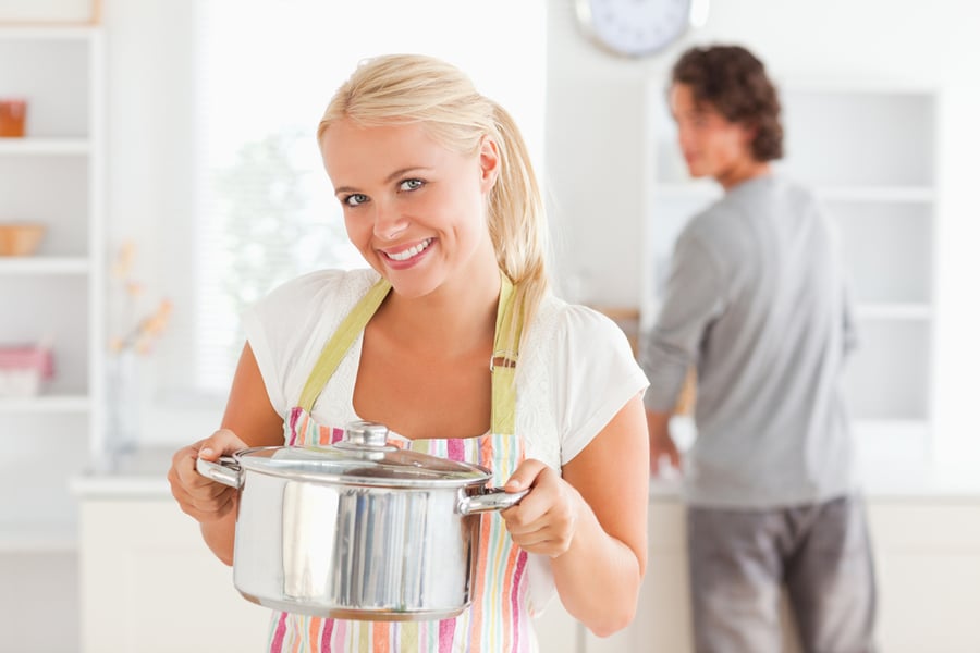 Woman posing with a boiler while her fiance is washing the dishes in their kitchen