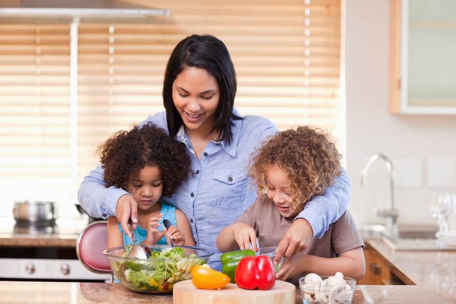 Young mother and daughters preparing salad in the kitchen together