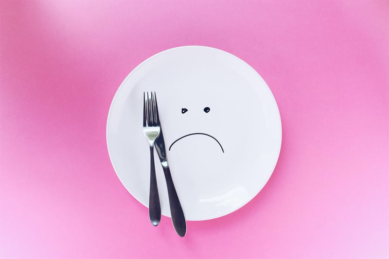 plate with sad face, knife and fork and pink background